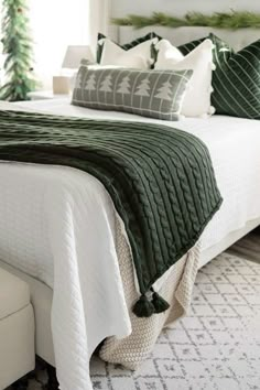 a white bed topped with green and white pillows next to a christmas tree covered headboard