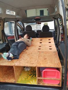 a man laying on top of a wooden table in the back of a van with its doors open