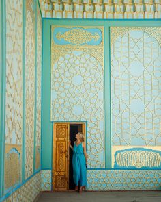 a woman in a blue dress standing at the entrance to a room with intricately painted walls