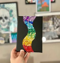 a hand holding up a piece of art that looks like a rainbow swirl on black paper