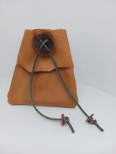 a brown leather bag with two metal handles and a button on the front, sitting on a white surface