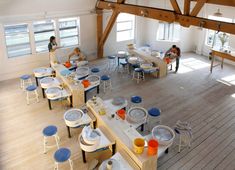 people are sitting at tables with plates and cups on them in an open room that has wooden beams