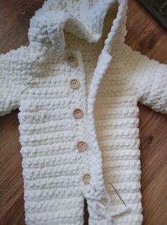 a white crocheted jacket with buttons on the collar and sleeves is laying on a wooden floor