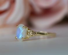 a close up of a ring on a table with flowers in the background and a pink rose behind it