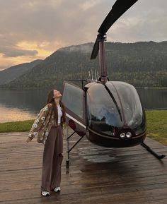 a woman standing in front of a helicopter on top of a wooden deck next to a lake