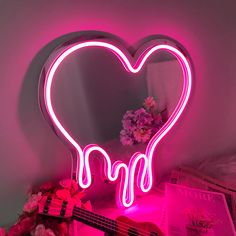 a pink neon heart shaped mirror sitting on top of a table next to a guitar