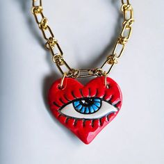 This unique necklace features a vibrant red heart-shaped ceramic pendant with a protective evil eye at its center, symbolizing love and protection. The pendant hangs from a durable stainless steel chain, making it both stylish and long-lasting. Perfect for those who appreciate handmade jewelry with a touch of symbolism, this piece is great for everyday wear or as a thoughtful gift. The combination of the red heart and evil eye brings together love, passion, and good fortune in a single beautiful accessory. Material : Stainless Stain Chain, Ceramic Evil Eye Length : 45 centimeters / 17.72 inches Unique Red Heart Shaped Jewelry, Unique Red Heart-shaped Necklace, Red Heart-shaped Necklaces With Charms, Red Heart Necklaces With Charms, Red Heart Pendant Necklace With Charms, Chain Ceramic, Heart Ceramic, Necklace Evil Eye, Protection Jewelry