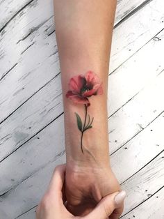 a woman's arm with a red flower tattoo on the left side of her wrist