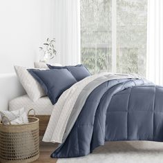 a bed with blue and white comforters in a room next to a basket on the floor