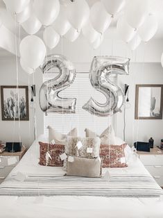 a bed topped with lots of white balloons next to a wall mounted number twenty five