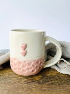 a white and pink coffee cup sitting on top of a wooden table next to a napkin