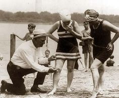 a group of people in bathing suits and hats on the beach with one man holding a rope