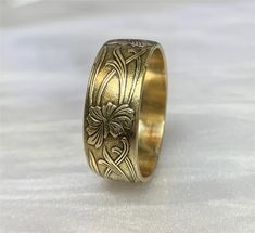 a gold wedding ring with an intricate design on the outside and inside, sitting on a white surface