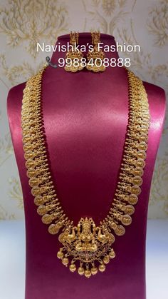 a gold necklace on display in front of a purple mannequin with an ornate design