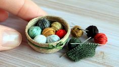 a small basket filled with balls of yarn next to a hand holding knitting needles and crochet hooks