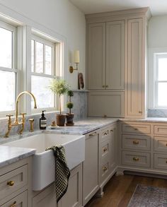 a kitchen with white cabinets and marble counter tops, gold faucets and brass pulls