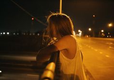 a woman standing on the side of a road at night with her arms behind her head