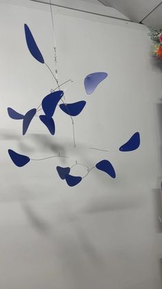 a wind chime hanging from the side of a white wall with blue leaves on it