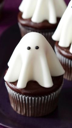 chocolate cupcakes decorated with white frosting and spooky ghost decorations on a purple plate