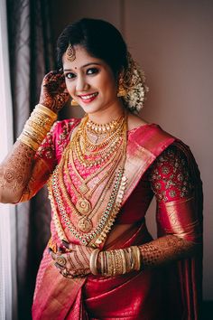 a woman in a red and gold sari with her hands on her head, smiling at the camera