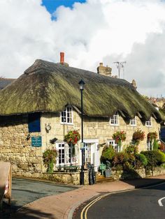 an old stone building with thatched roof and flowers growing on the windows, next to a street light