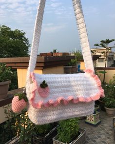 a crocheted purse hanging from a roof with potted plants in the background