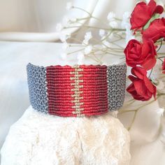 a red, white and blue bracelet sitting on top of a rock next to flowers