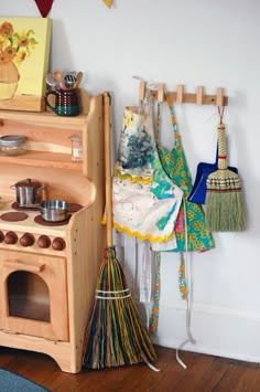 an old fashioned wooden toy stove with brooms and pots on the rack next to it