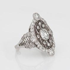 Stylish antique Edwardian diamond crafted in 900 platinum (circa 1910s).   Center set old European cut diamond is estimated at 0.75 carats (estimated at I-J color and VS2 clarity). Old European cut diamonds surround the center diamond and total an estimated 0.67 carats (estimated at I-J color and SI1-I1 clarity). The total diamond weight is estimated at 1.42 carats.   This one is for the books! A spectacular Edwardian era dinner ring highlights a bright and lively center set old European cut diamond, with a surround of shimmery diamonds set into an open work lattice mount. The cocktail ring is larger in scale (north to south measuring 24mm - 0.94 inches) and makes a great statement on the hand. The low rise ring (4.5mm - 0.17 inches) sits flat and comfortably on the finger. The original Ed Edwardian Diamond Ring, Edwardian Era, European Cut Diamonds, Cocktail Rings, Diamond Ring, Platinum, Diamond Cuts, Ring Size, Fine Jewelry