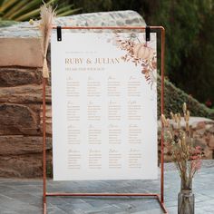 a wedding seating chart is displayed on a metal stand next to some flowers and greenery