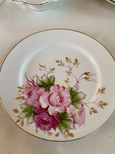 a plate with pink flowers on it sitting on top of a white tablecloth covered table