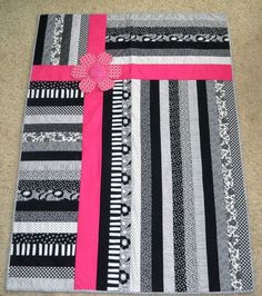 a black and white quilt with pink ribbon on the front, sitting on top of a carpet