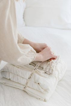 a woman sitting on top of a pile of white blankets next to a stack of pillows