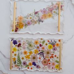 two pieces of glass with flowers painted on them sitting on a marble counter top next to each other