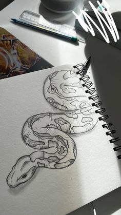 a drawing of a snake on top of a book next to a cup and pen