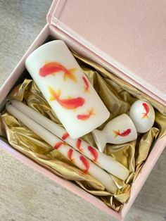 four candles in a pink box with gold foil and red fish on them, sitting next to each other