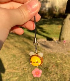 a hand holding a keychain with a bee on it's face and flower in its mouth