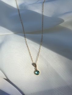 a necklace with a blue stone on it sitting on top of a white cloth covered sheet