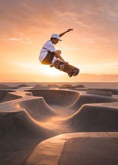 a man flying through the air while riding a skateboard in a skate park at sunset