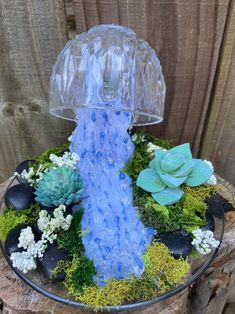 a glass water fountain surrounded by succulents and moss on a tree stump