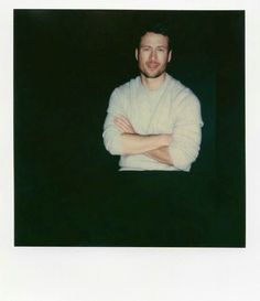 a man with his arms crossed standing in front of a black background and looking at the camera