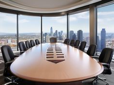 an empty conference table with black chairs in front of large windows overlooking cityscape