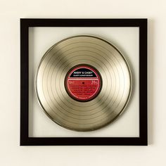 a gold record in a black frame on a white wall with a red label underneath it