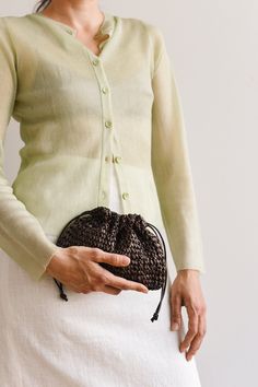 a woman wearing a white skirt and green cardigan holding a black purse in her hands