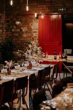 a long table is set with wine glasses and flowers in front of a brick wall