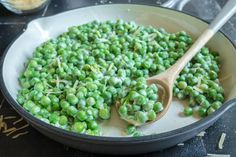 peas are being cooked in a pan with a wooden spoon