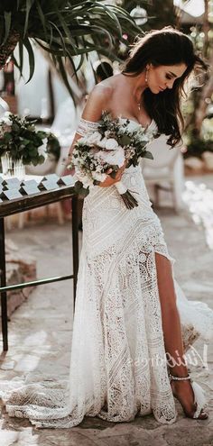 a woman in a white dress is standing near a table with flowers and greenery