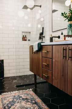 a bathroom with black and white tile, wooden cabinetry, rug, and mirror