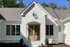 a white brick house with a clock on the front door and two windows above it