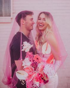 a man and woman standing next to each other with pink flowers in front of them